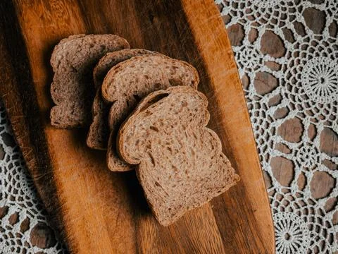 Stack of Wholegrain Bread Slices on Rustic Wooden Board with Lace Tablecloth Stock Photos