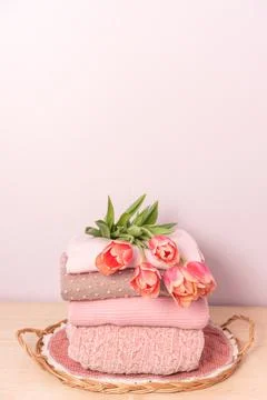 A stack of womens knitted sweaters on a wicker tray on a shelf, next to a bou Stock Photos