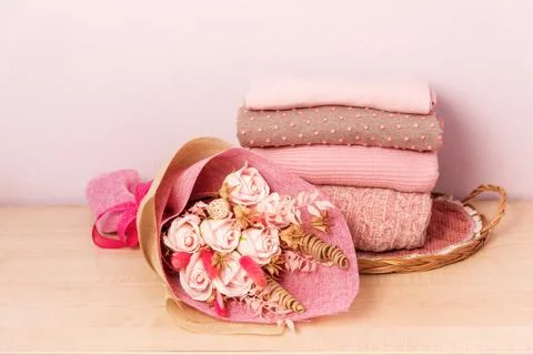 A stack of womens knitted sweaters on a wicker tray on a shelf, next to a bou Stock Photos