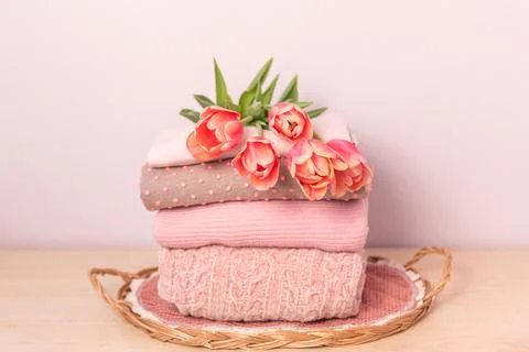 A stack of womens knitted sweaters on a wicker tray on a shelf, next to a bou Stock Photos