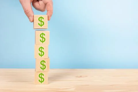 Stack of wooden block cube with dollar sign on table, blue background. copy s Stock Photos