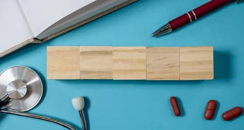 Stack of wooden blocks sits on a blue surface next to a pen and a stethoscope Stock Photos