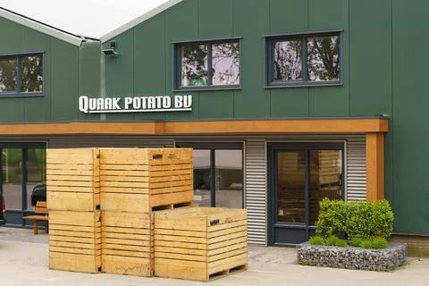 A Stack of Wooden Crates Outside a Green Building With the Sign Quark Potato Stock Photos