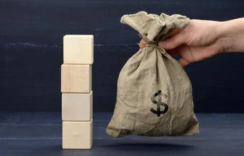 A stack of wooden cubes and a woman's hand holds a full bag with a dollar sig Stock Photos
