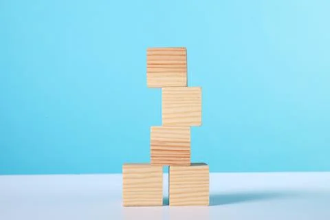 Stack of wooden cubes on white table against light blue background Stock Photos