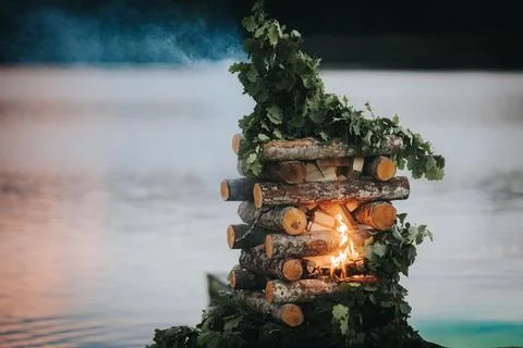 Stack of wooden logs adorned with green leaves burning brightly near a calm.. Stock Photos