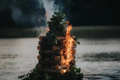 Stack of wooden logs burning with flames and smoke rising above water, surr.. 写真素材