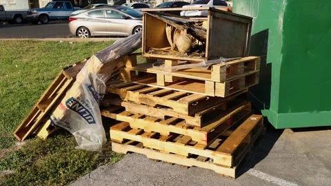 Stack of wooden pallets and discarded materials beside large green dumpster Video stock 321324777