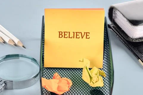 A stack of yellow sticky notes with the word BELIEVE sits within a black mesh Stock Photos