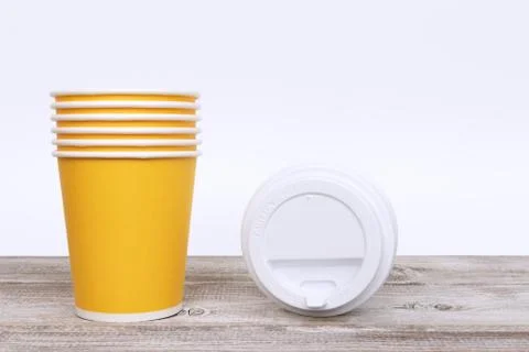 A stack of yellow take away disposable paper cups and plastic caps on wooden  库存照片