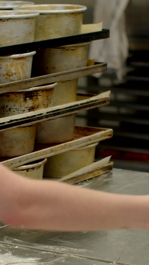 Stacked baking pans and trays on worn metal tabletop in commercial kitchen Stock Footage 345601426