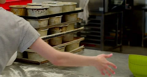 Stacked baking pans and worker staging trays on stainless prep table in, with Stock Footage 344596433