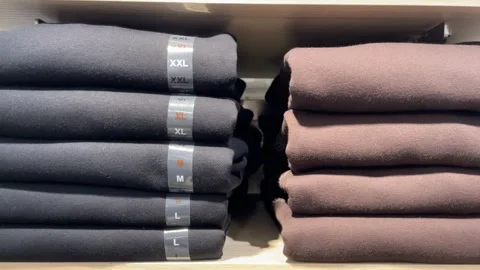 Stacked black and brown folded sweatshirts on wooden shelf in retail store .. Stock Footage 332064219