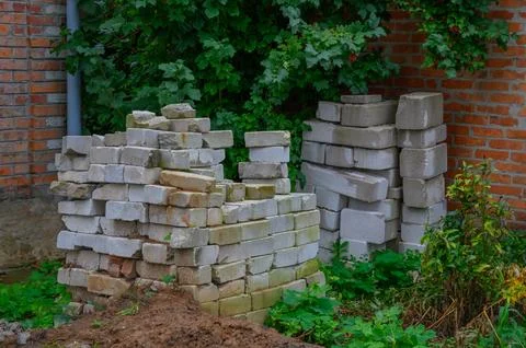 Stacked bricks and concrete blocks near a brick wall in a backyard garden Stock Photos