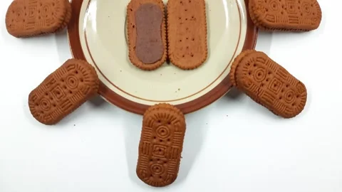 Stacked chocolate cream filled biscuits arranged artistically around a plate Stock Footage 329225275