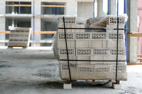 Stacked construction bricks on pallet inside unfinished building site Stockfoto's