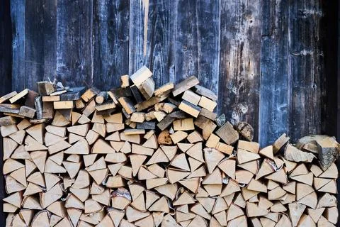 Stacked firewood placed against rustic wooden wall. Close up of chopped logs  Stock Photos