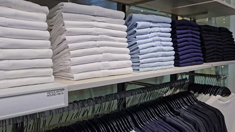 Stacked folded shirts in white, light blue, and navy colors on store shelf Stock Footage 313149100