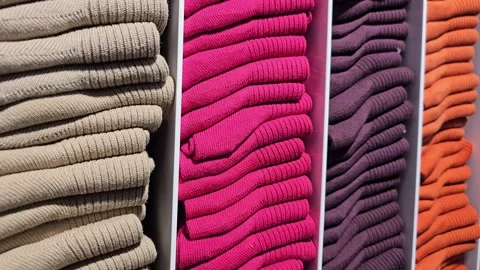 Stacked folded sweaters in beige, pink, purple, and orange colors on shelves Video stock 300299203