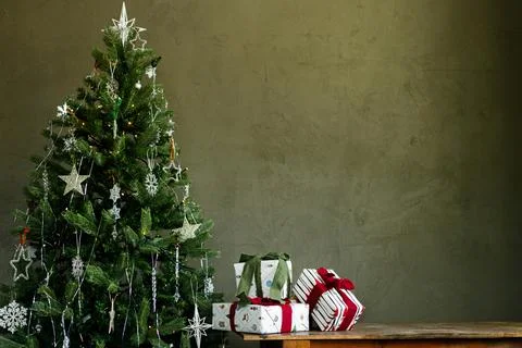 Stacked Gift Boxes with Red and Green Ribbons Placed Beside a Glowing Tree Stock Photos
