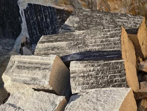 Stacked grooved granite stone blocks at quarry showing weathered surfaces, dust, Stock Photos