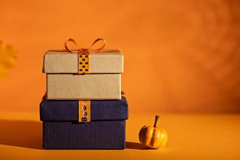 Stacked Halloween gift boxes with mini pumpkin on orange background for sea.. Stock Photos