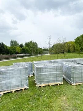 Stacked pallets of tiles for pedestrian path repair in a park, surrounded by Stock Photos