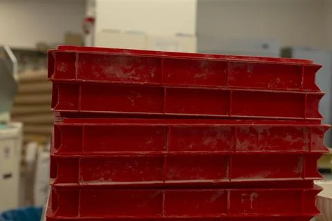 Stacked red plastic crates in worn workshop storage area with scuffed surfaces Stock Photos