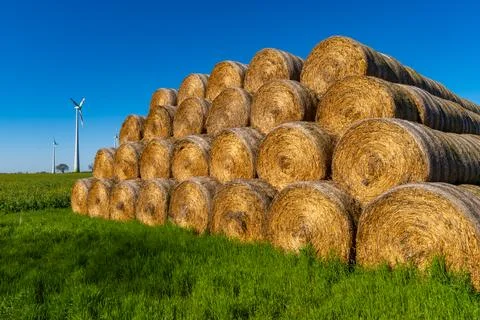 Stacked Round Straw Bales with Wind Turbines in a Sustainable Farming Landsca Stock Photos
