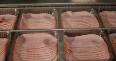 Stacked slices of ham lie in clear plastic trays on a production line in a meat Stock Footage 339992095