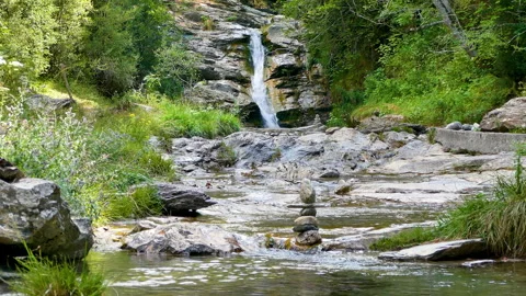 Stacked stones in a mountain stream with a small waterfall in the background. Video stock 308162708