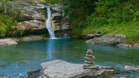 Stacked stones in a mountain stream with a small waterfall in the background. Stock Footage 312004876
