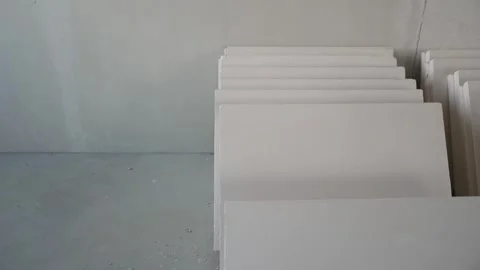 Stacked white drywall panels on concrete floor during renovation Stock Footage 334449083