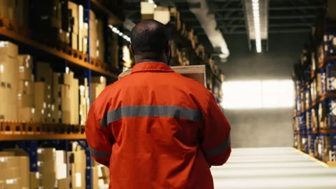 Stacking cargo pallets, black warehouse worker, in distribution hub space Stock Footage 332910810