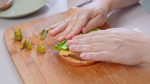 Stacking lettuce and a grilled beef patty onto a cheeseburger on a wooden boa Stock Footage 347182674