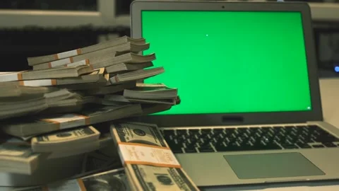 Stacks 100 US dollars bills and laptop with green screen in office night time. Stock Footage 248104098