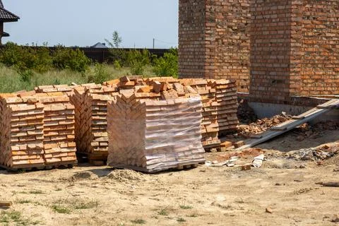 Stacks of clay bricks sit on pallets near a half-built brick wall at a cons.. Stock-Fotos