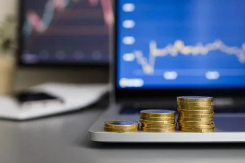 Stacks of coins against the background of growing income graphs on monitors Stock Photos