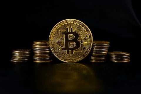 Stacks of coins and in between a gold coin bitcoin on black leather Stock Photos