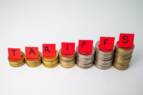 Stacks of coins and "tariffs" text. Increase in tariffs and costs. Stock Photos