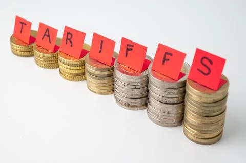 Stacks of coins and "tariffs" text. Increase in tariffs and costs. Stock Photos