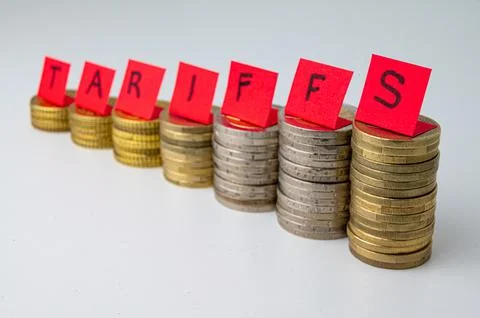 Stacks of coins and "tariffs" text. Increase in tariffs and costs. Stock Photos