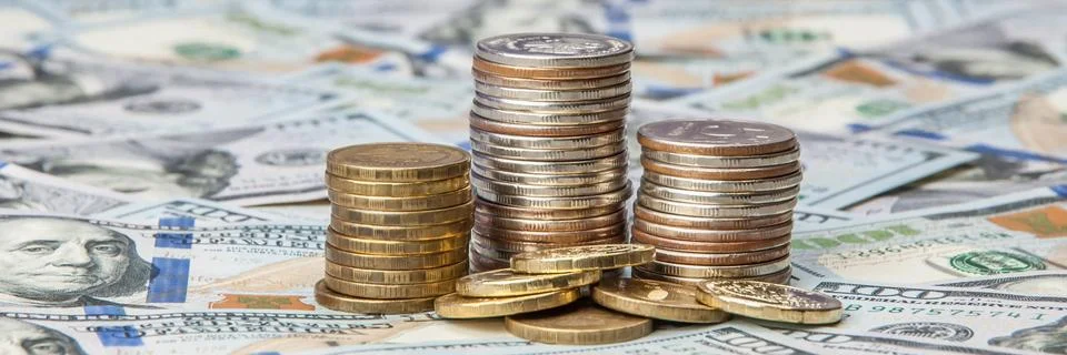 Stacks of coins on the scattered notes of dollars on a brilliant background. Stock Photos