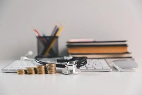 Stacks of coins with stethoscope, computer keyboard and books on office des.. 写真素材