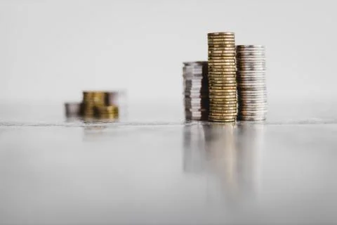 Stacks of different coins divided between a small and a big group on white ba Stock Photos
