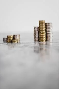 Stacks of different coins divided between a small and a big group on white ba Stock Photos