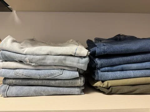 Stacks of folded denim jeans organized on a wardrobe shelf  Stock Photos