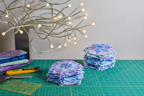 Stacks of hexagonal patchwork blocks, quilting accessories, table lamp on a.. Fotos de archivo