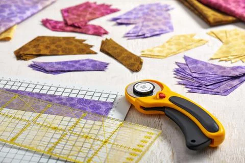 Stacks of multi-colored pieces of fabric, cutting mat, ruler, rotary cutter Stock Photos