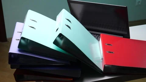 Stacks of multicolored ring binders and a laptop on a desk showing office Stock Footage 346250212